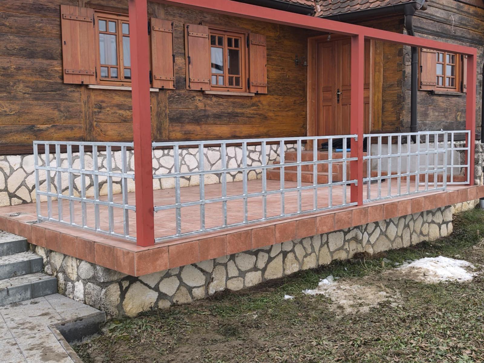 Pocinčana ograda terase drvene kuće s crvenim čeličnim stupovima nadstrešnice.